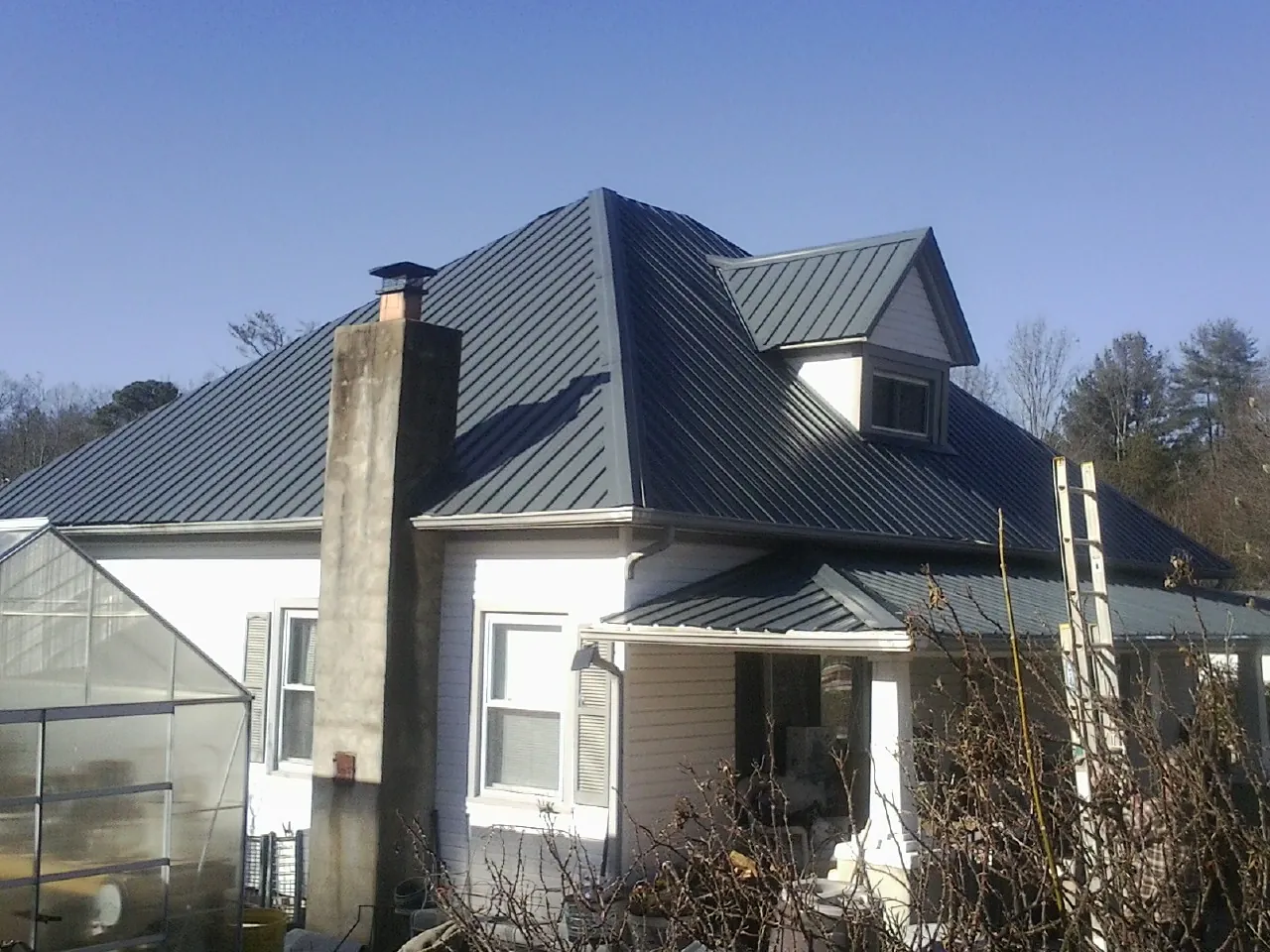 Dark blue standing seam metal roof on a white farmhouse with dormer — Slate & Tile Roof Repair by Roofing Brothers in Mendenhall