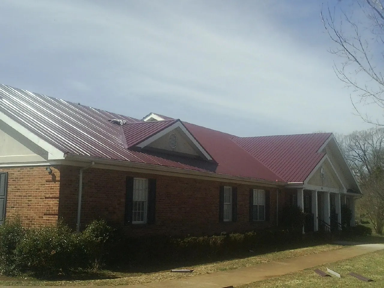 Red metal roof with gabled entries on a long brick building, from a Hail Damage Roof Repair job in Mendenhall