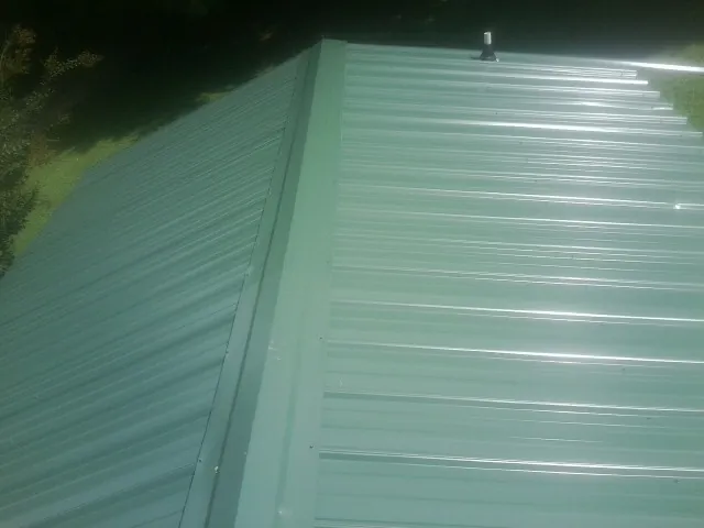 New green metal panels meeting at the ridge of a roof — Flat Roof Repair work by our crew in Mendenhall