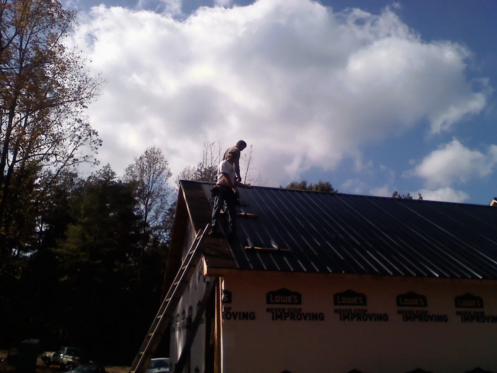 Roofer fastening dark metal panels high against a cloudy sky, from a Roof Inspection job in Mendenhall