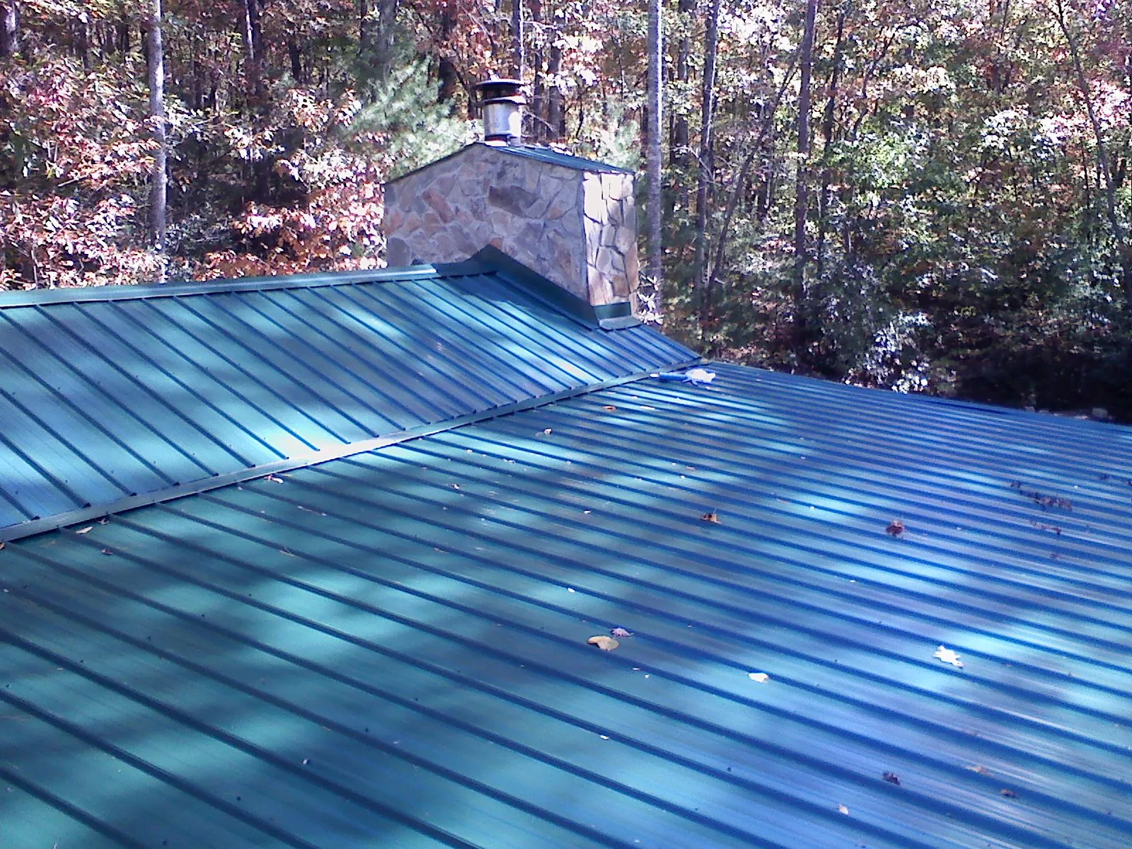 New green metal roof and stone chimney surrounded by autumn woods in Mendenhall