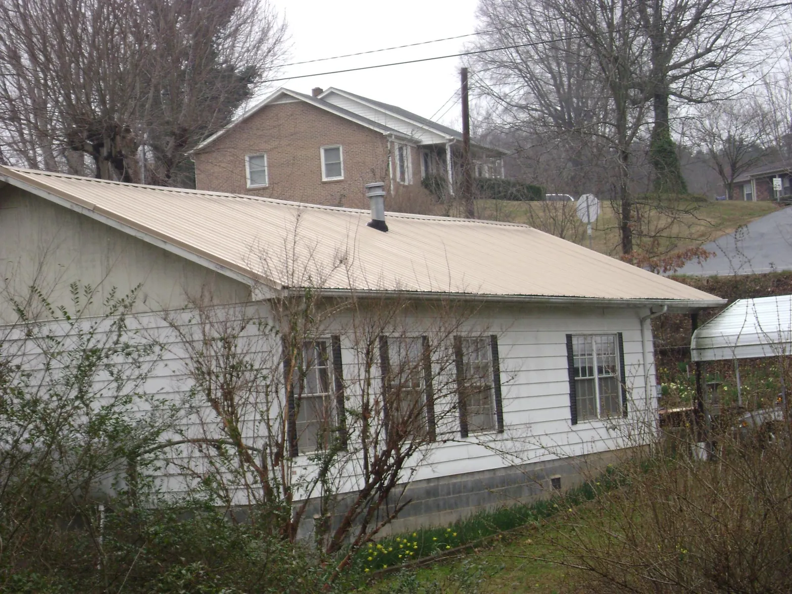 Tan metal roof on a white sided house set into a hillside — Commercial Roofing by Roofing Brothers in Mendenhall