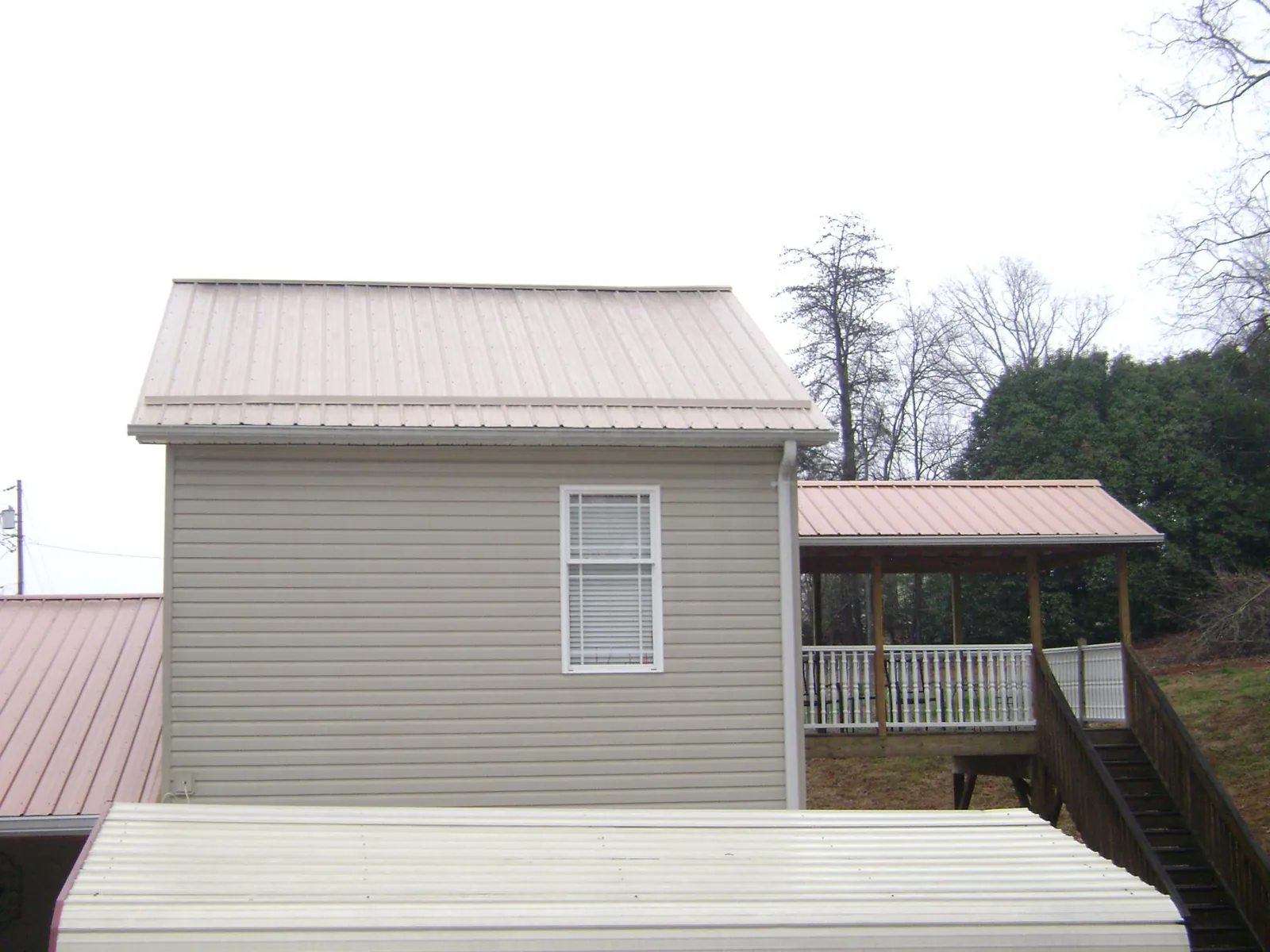 Tan metal roofs on a two story addition and attached porch, from a Roof Replacement job in Mendenhall